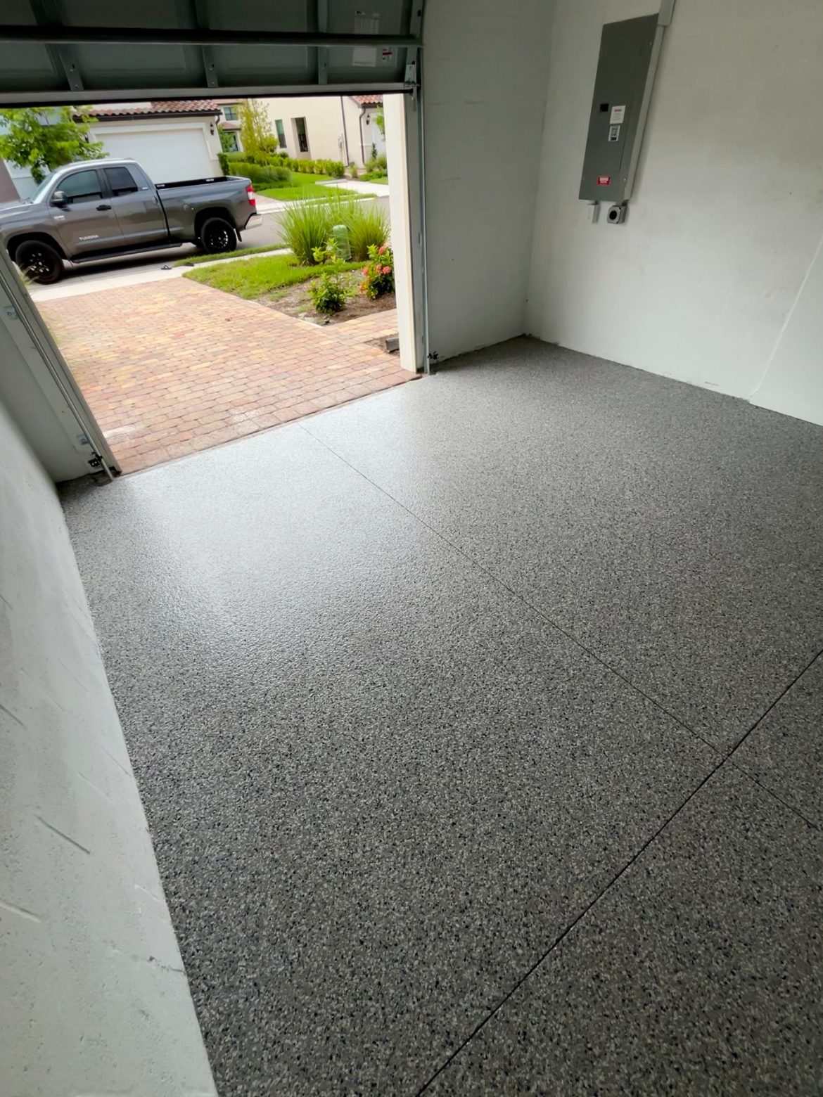 Decorative flake epoxy garage floor looking out the open garage door toward the paver driveway